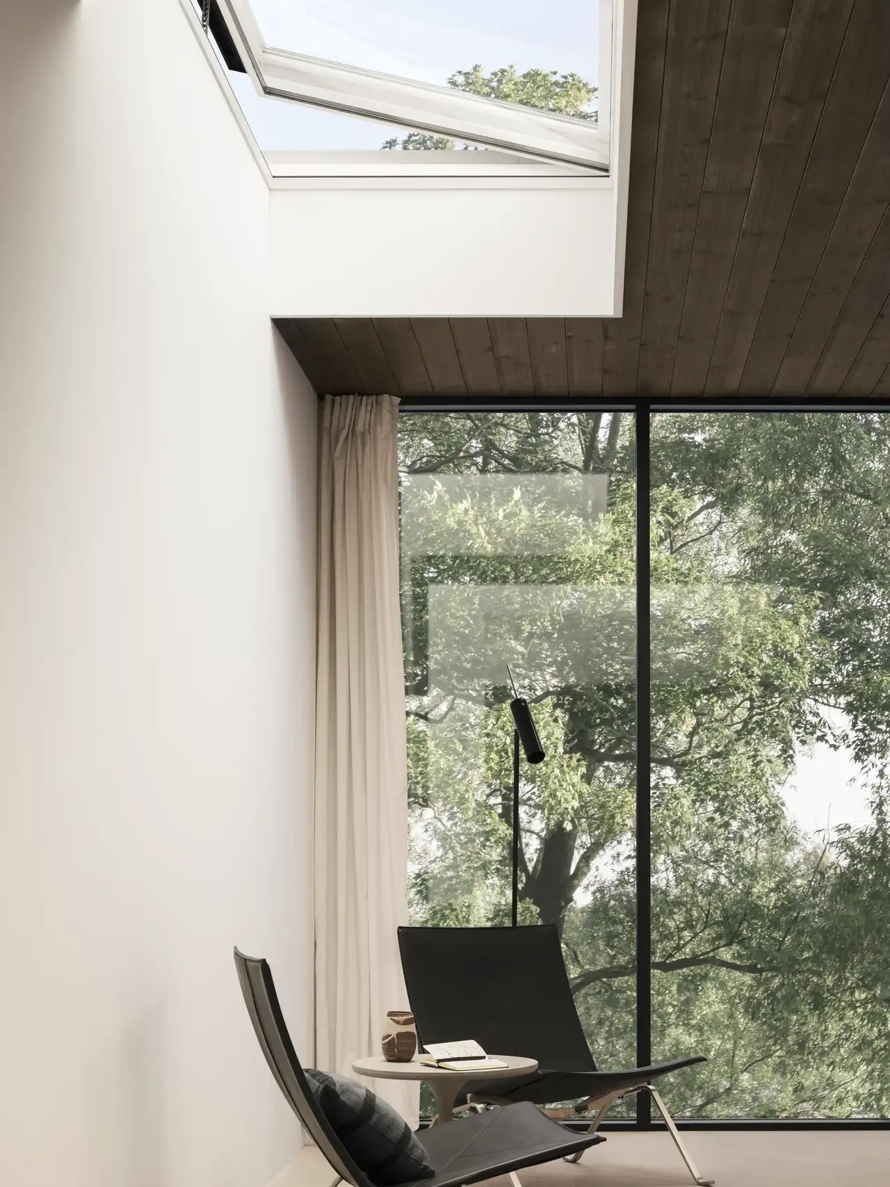 Deux fauteuils et une table basse près d’une grande fenêtre verticale et sous une fenêtre de toit plate ouverte.