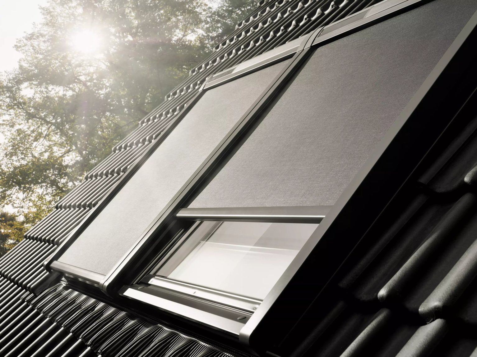 VELUX roof window with sunshade on a steeply pitched black tile roof.
