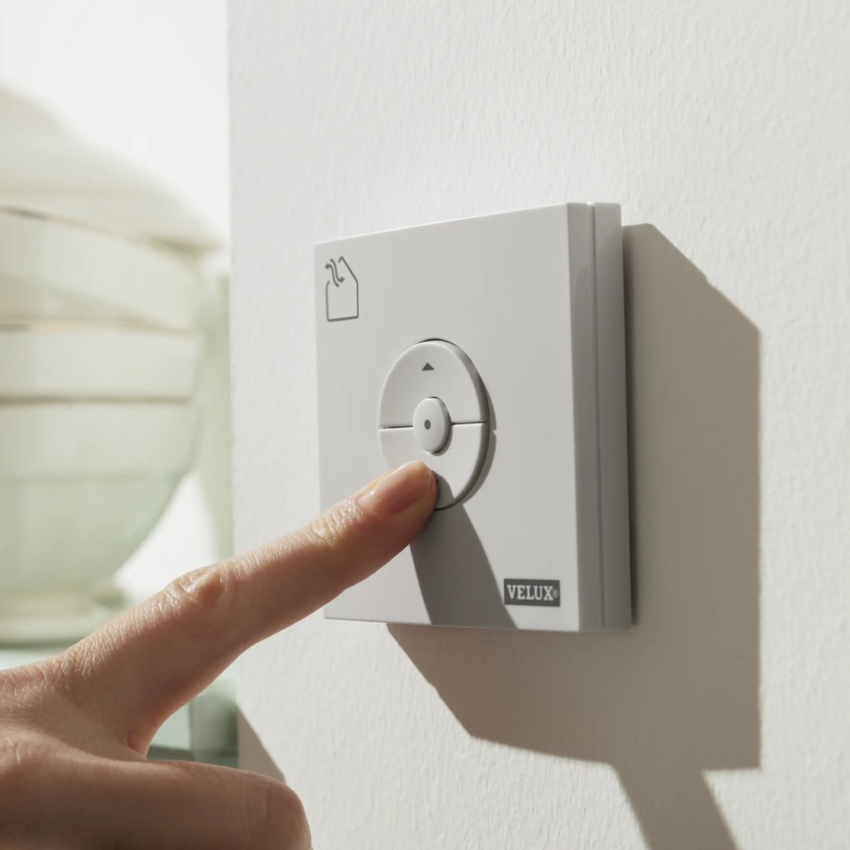 Hand pressing VELUX remote control button in kitchen.