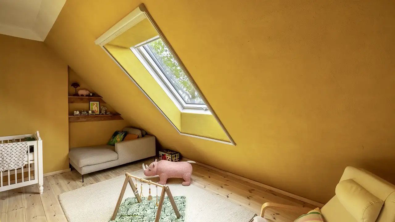 Ein helles Dachkinderzimmer mit warmen gelben Wänden, einem weichen Teppich und einer Spielecke, durchflutet von Tageslicht durch ein VELUX Dachfenster. | VELUX Magazin