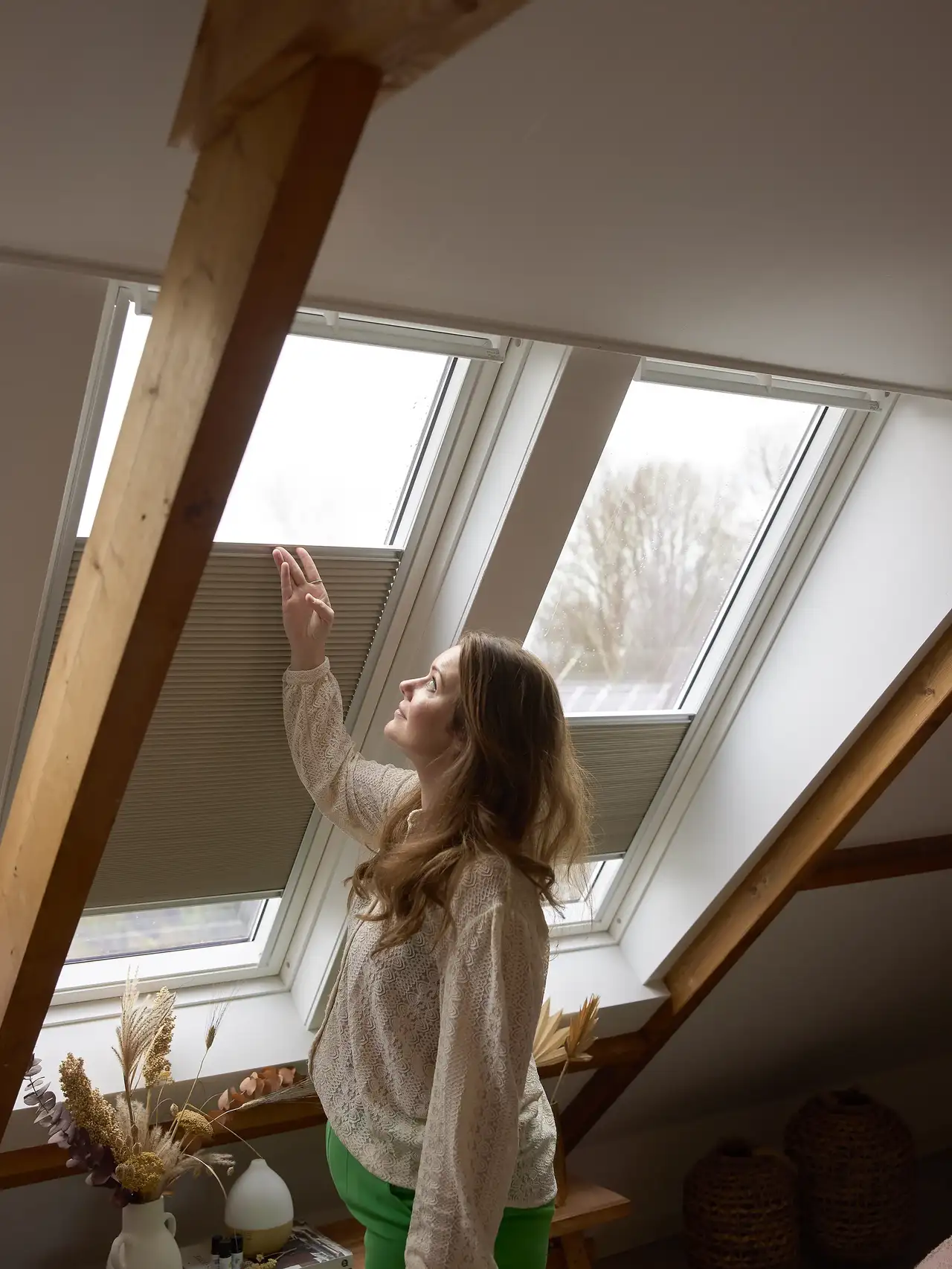 Une femme règle la position des stores plissés occultants sur des fenêtres de toit VELUX. 