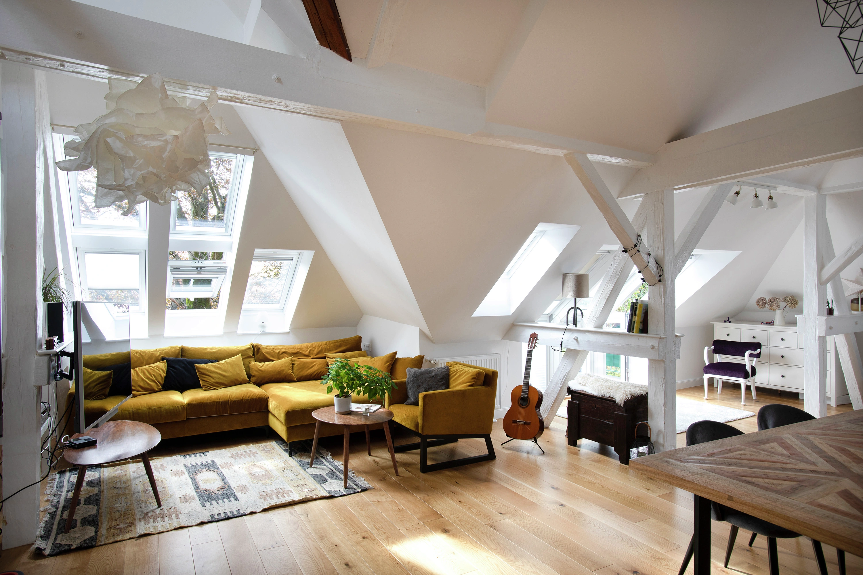 Bēniņu dzīvojamā istaba ar slīpiem griestiem, VELUX jumta logiem un mājīgām mēbelēm.