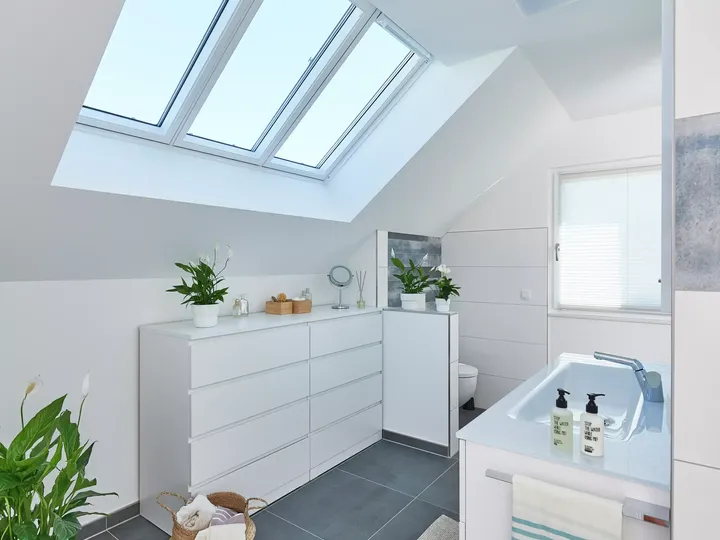 Modernes Badezimmer mit weißen Schränken und VELUX Dachflächenfenstern, die Sonnenlicht hereinlassen.