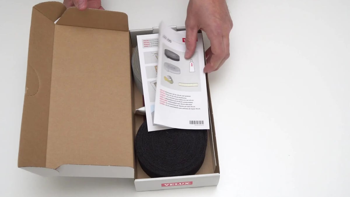 Person installs VELUX roof window using tools from a package.