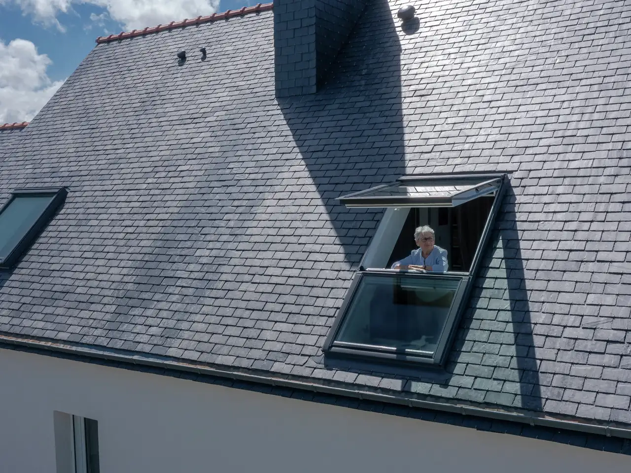 Vista dall’esterno: signora anziana guarda fuori dal suo balcone sul tetto Rivista VELUX