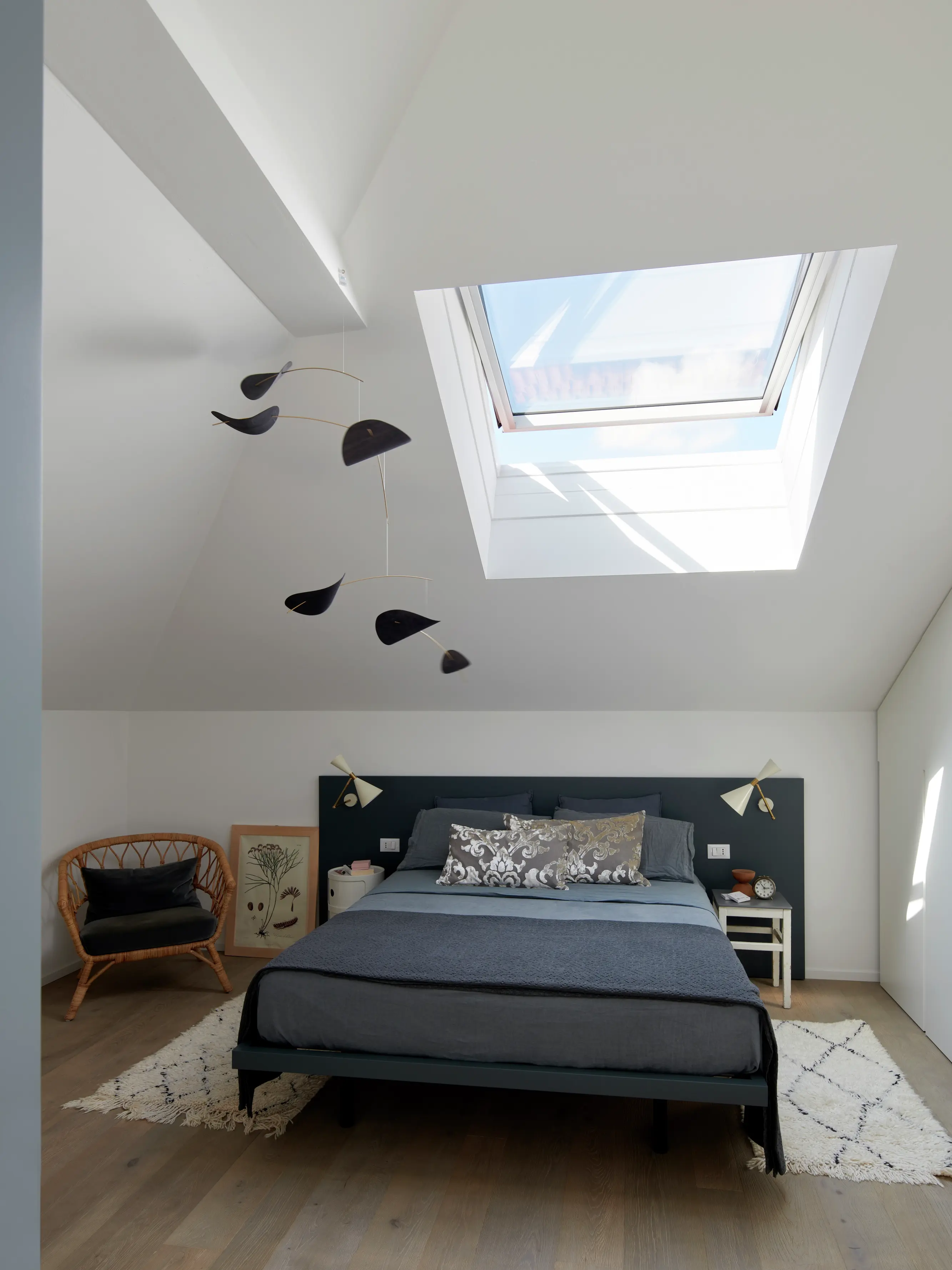 Une chambre mansardée moderne avec un lit bleu canard, un puits de lumière et un décor minimaliste