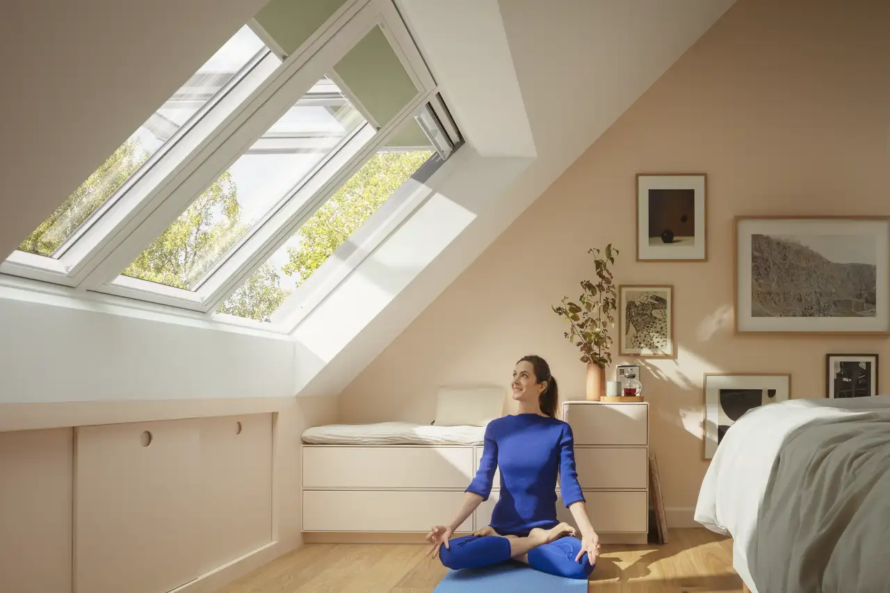 Femme en méditation dans une mansarde baignée de lumière naturelle grâce aux fenêtres de toit. 