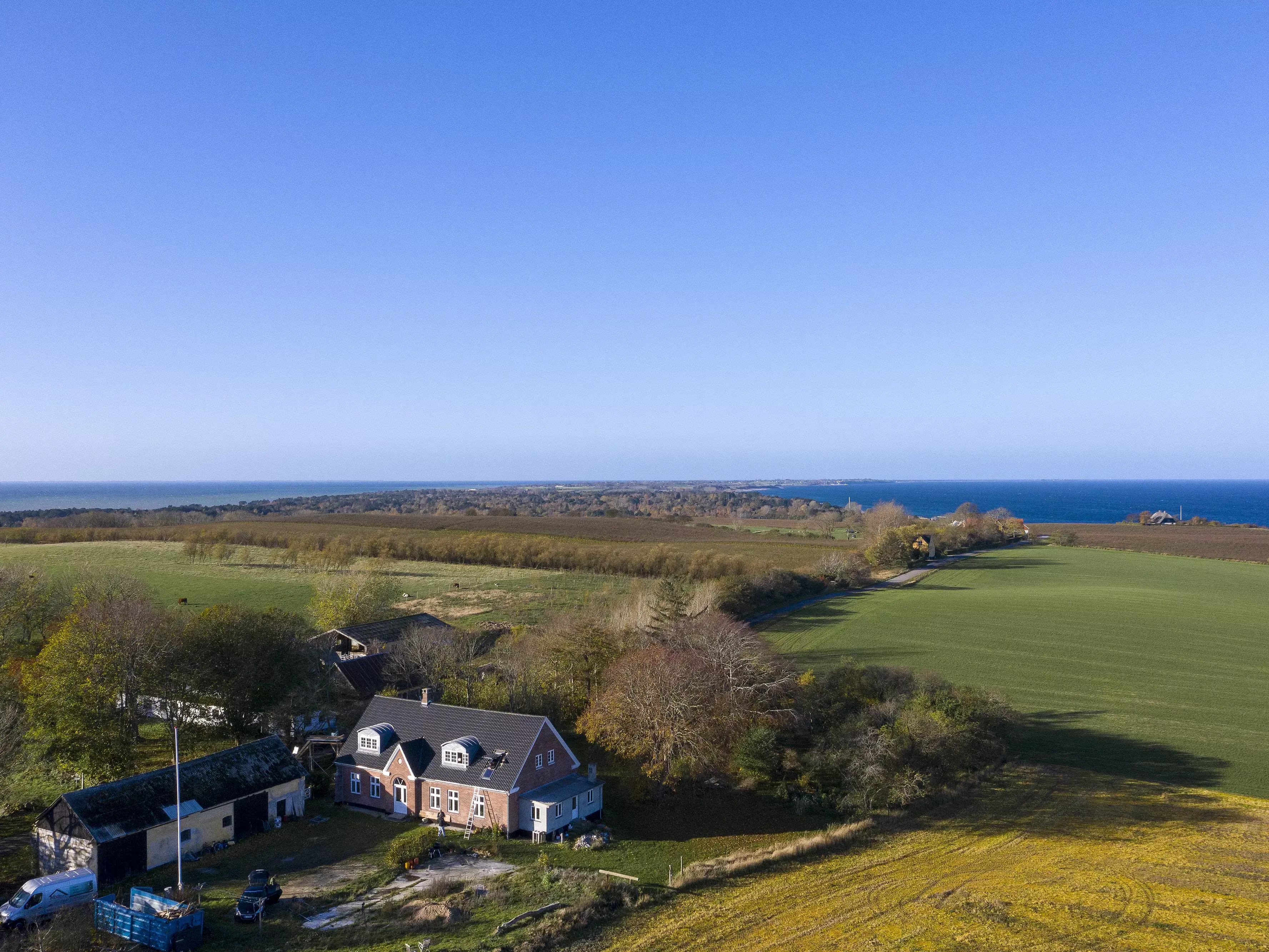 Vue aérienne d'une maison individuelle en campagne près de la mer avec des champs verts aux alentours.