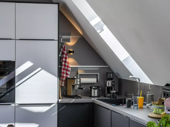 Moderne Küche mit grauen Schränken und einem VELUX Dachflächenfenster, durch das Sonnenlicht einfällt.