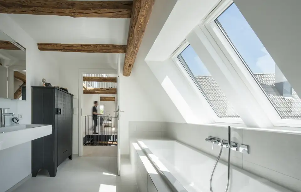 Grande salle de bain mansardée avec deux fenêtres de toit côte à côte au-dessus de la baignoire.