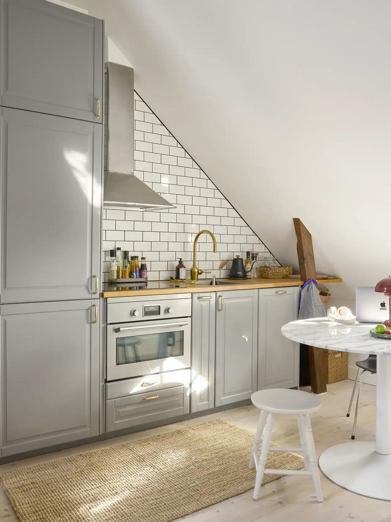 Cucina in mansarda con ante grigie, piano in legno e paraschizzi bianco tipo metro illuminato da finestra per tetti