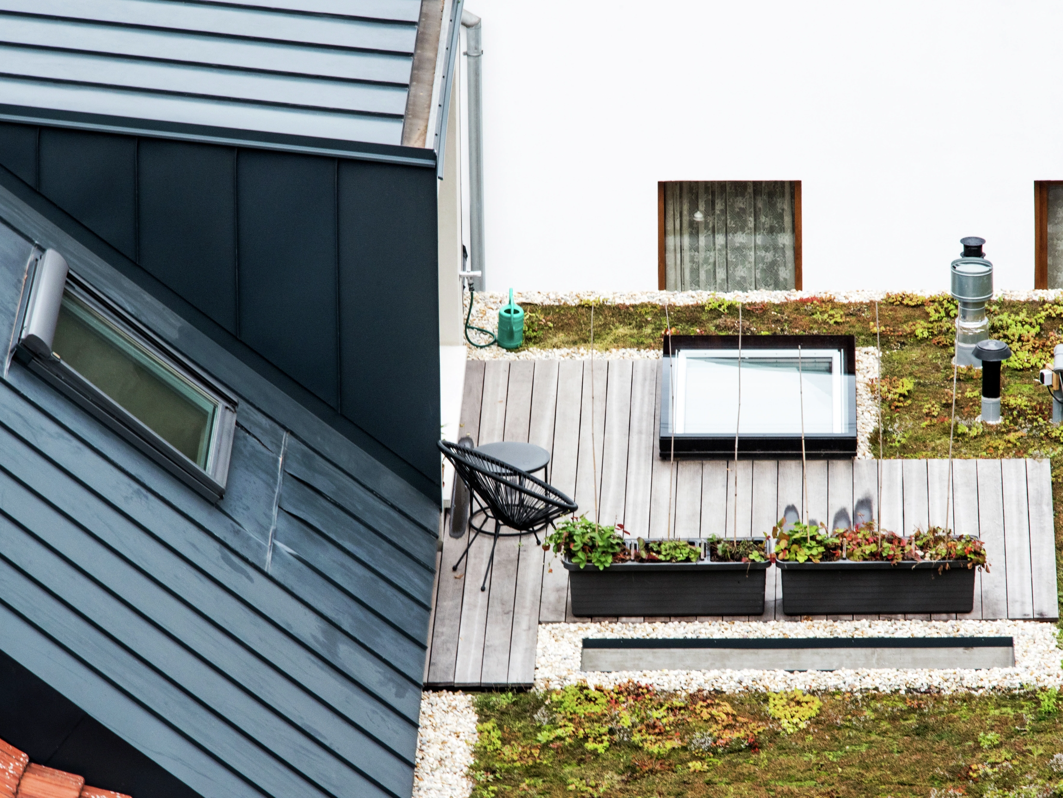 Tetto moderno con una piccola terrazza in legno con finestra per tetti piani VELUX e una parte ricoperta di vegetazione.