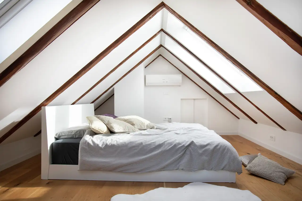 Cozy bedroom featuring a bed with decorative pillows, sloped roof beams, and roof windows allowing natural light. | VELUX