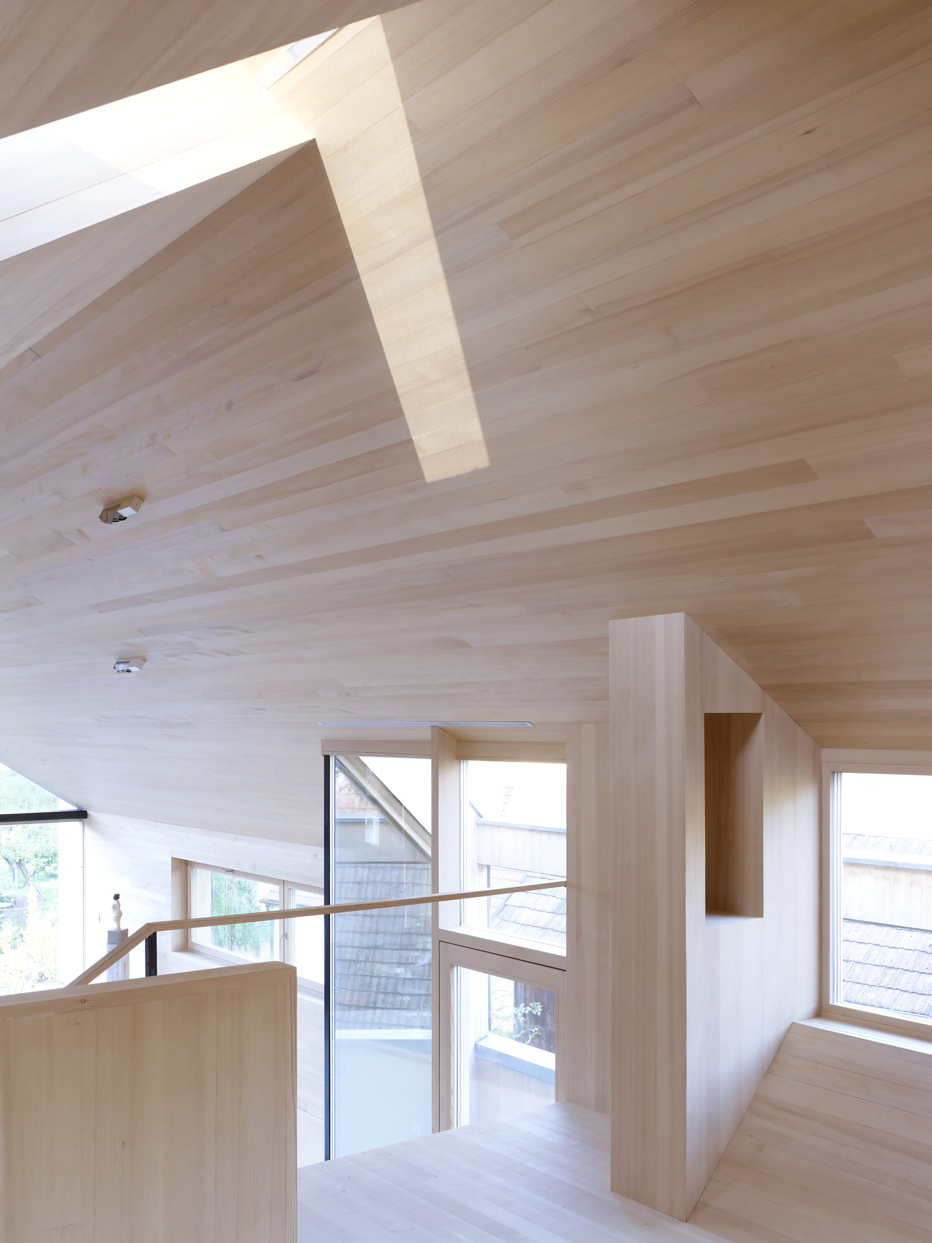 Mansardă modernă cu interior din lemn și ferestre mari, care pătrund în lumină naturală.
