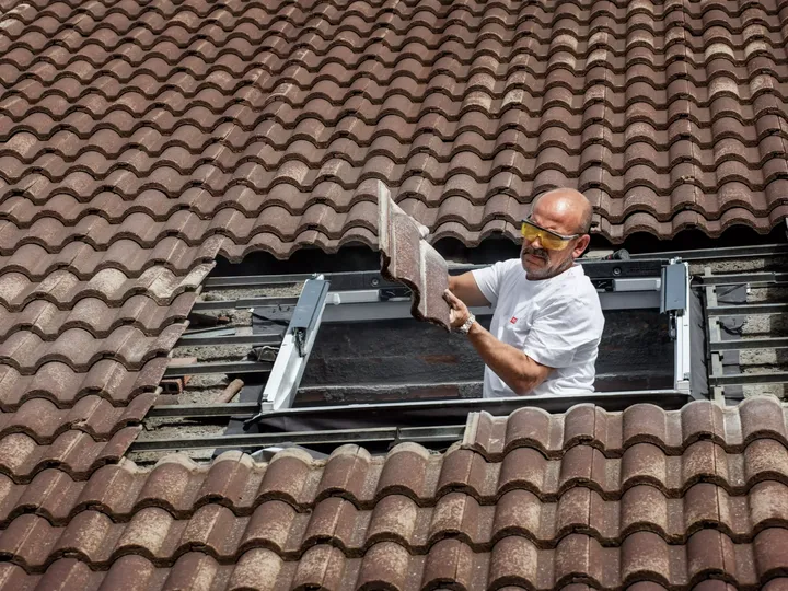 Einbauer, der ein VELUX Dachflächenfenster in ein Ziegeldach einbaut, um die Raumbeleuchtung zu verbessern.