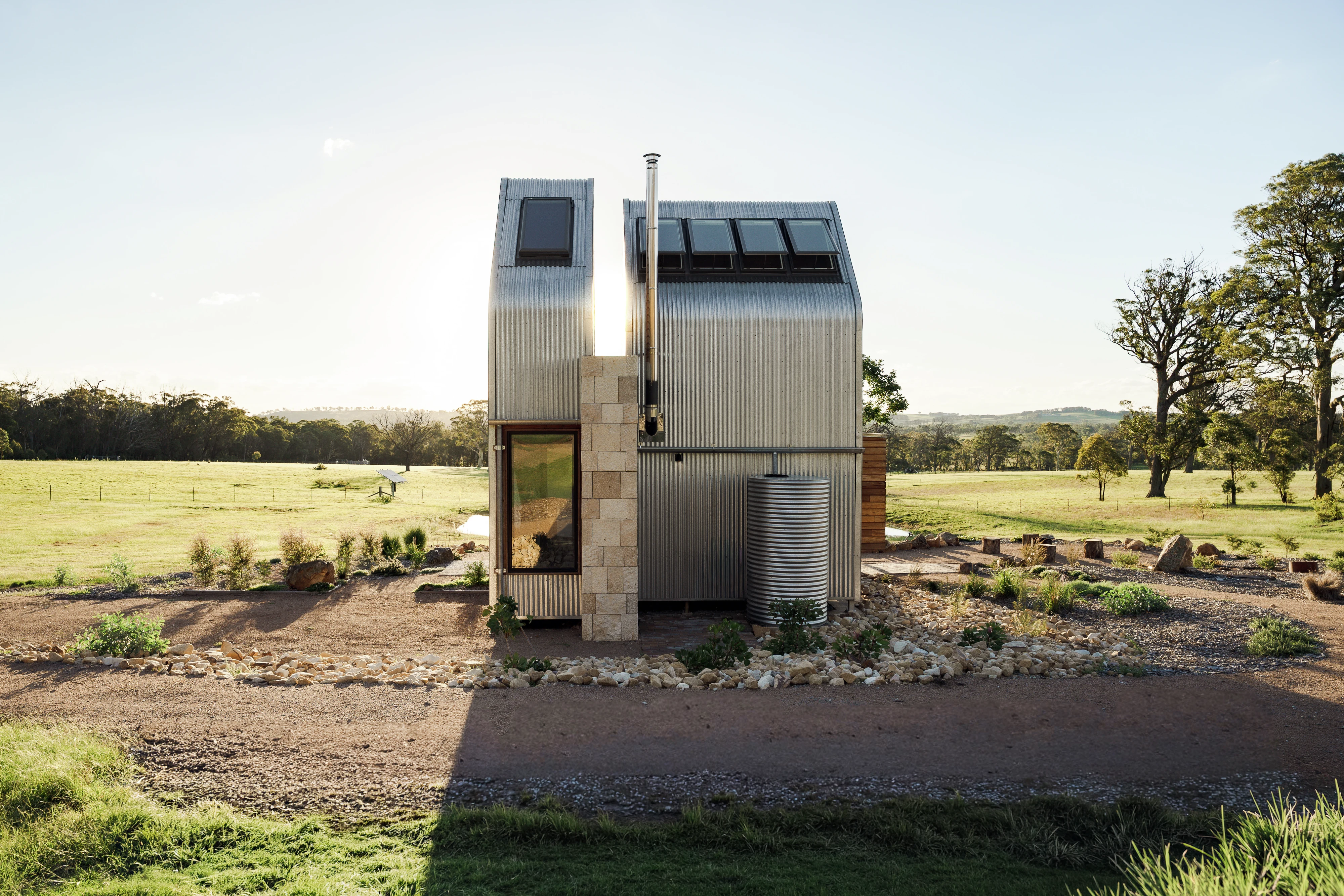 Tiny metal-clad house with VELUX roof windows in a sunny rural landscape.