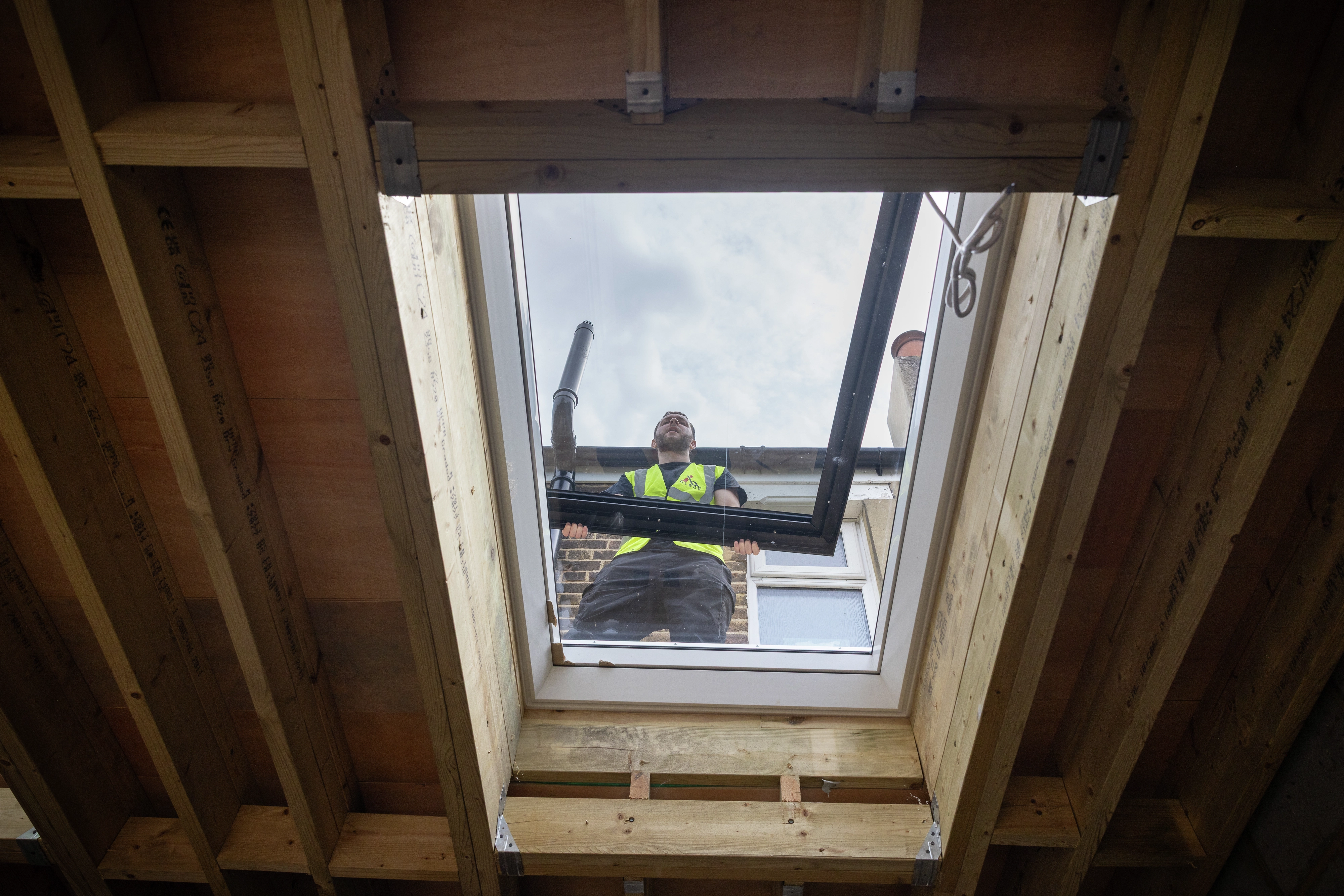 Installer in hi-vis opening a VELUX flat roof window above exposed timber joists.