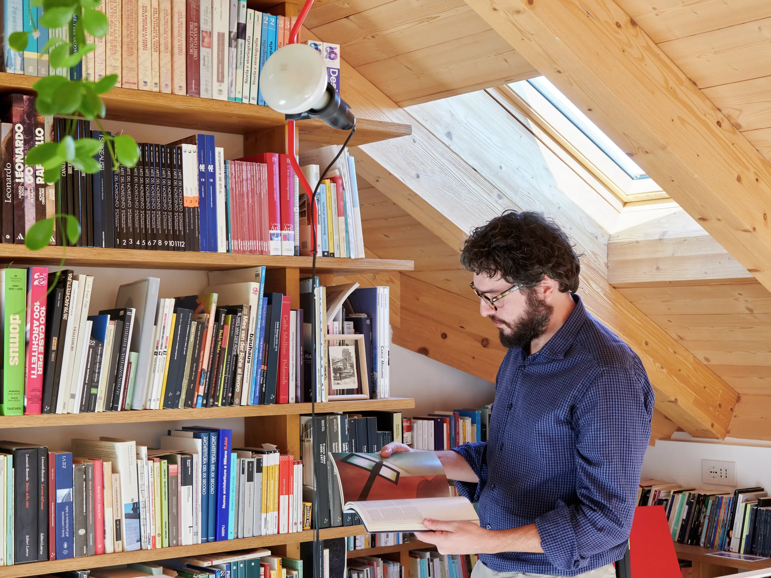 Espace de lecture dans le comble avec des étagères, une fenêtre de toit VELUX et une personne en train de lire.