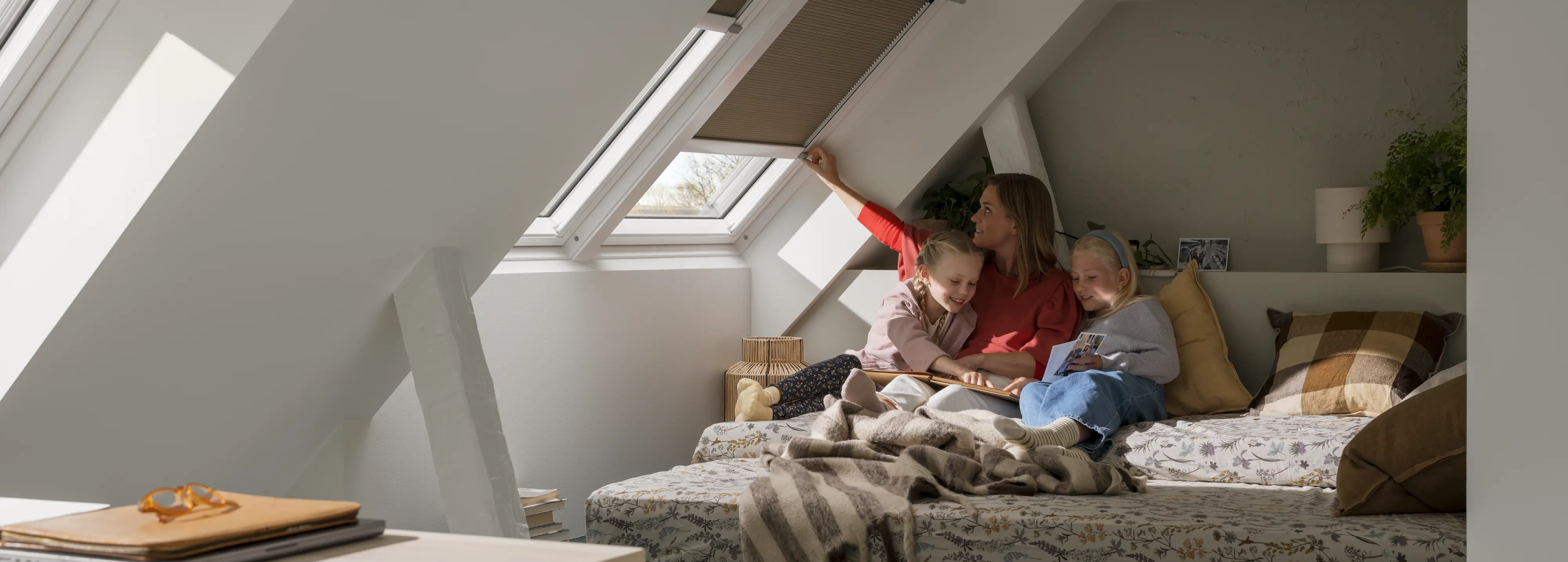 Attic room with VELUX roof windows and blind, sleeping area with woman and girls, natural light.