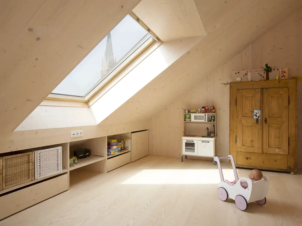 La lumière de la grande lucarne éclaire la poussette en bois dans la chambre d'enfant | Magazine VELUX