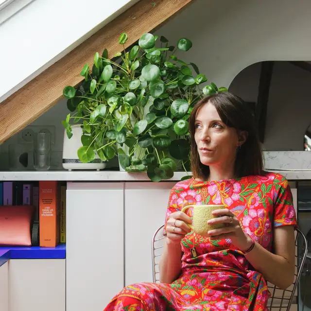 Kobieta w kwiecistej sukience trzymająca filiżankę herbaty przy oknie dachowym. | VELUX