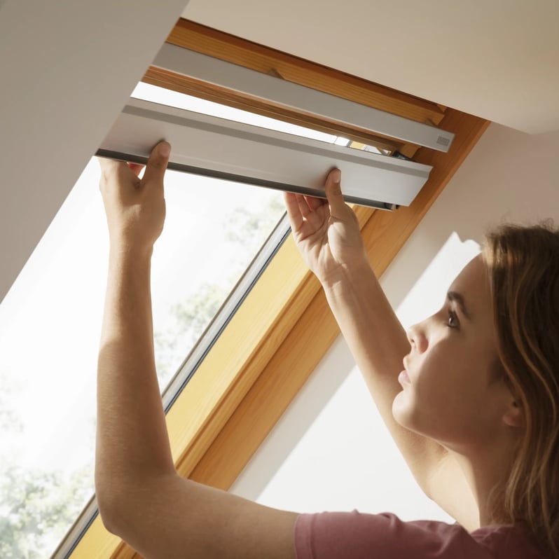 Person opening a VELUX roof window, allowing light and air inside.