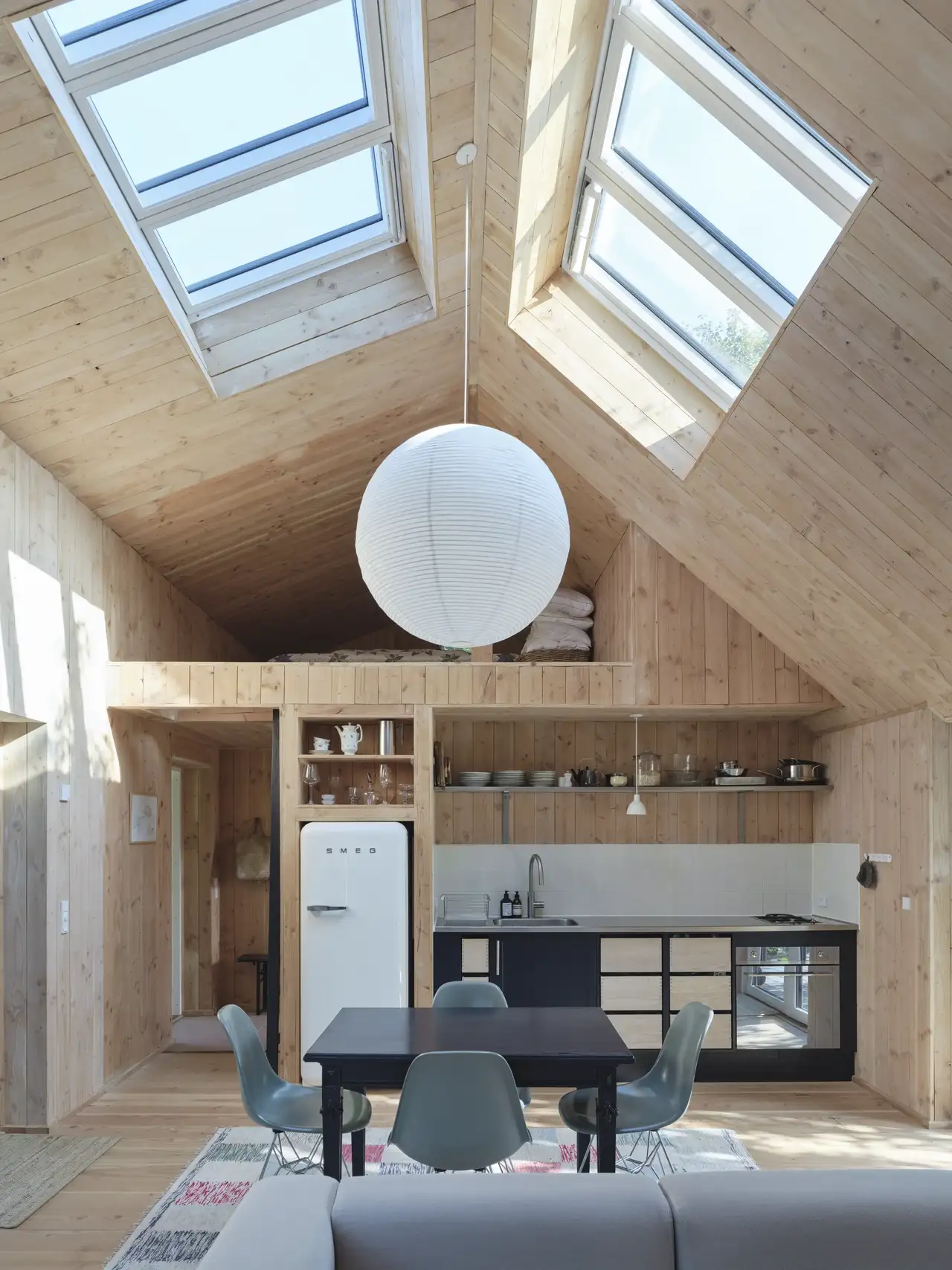 Cucina moderna aperta su soggiorno con soffitto spiovente in legno, soppalco e finestre per tetti VELUX