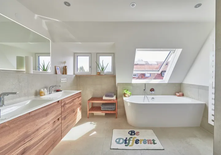 Helles, modernes Badezimmer mit VELUX Dachflächenfenster, freistehender Badewanne, hölzernem Waschtisch und 'Be Different' Matte.