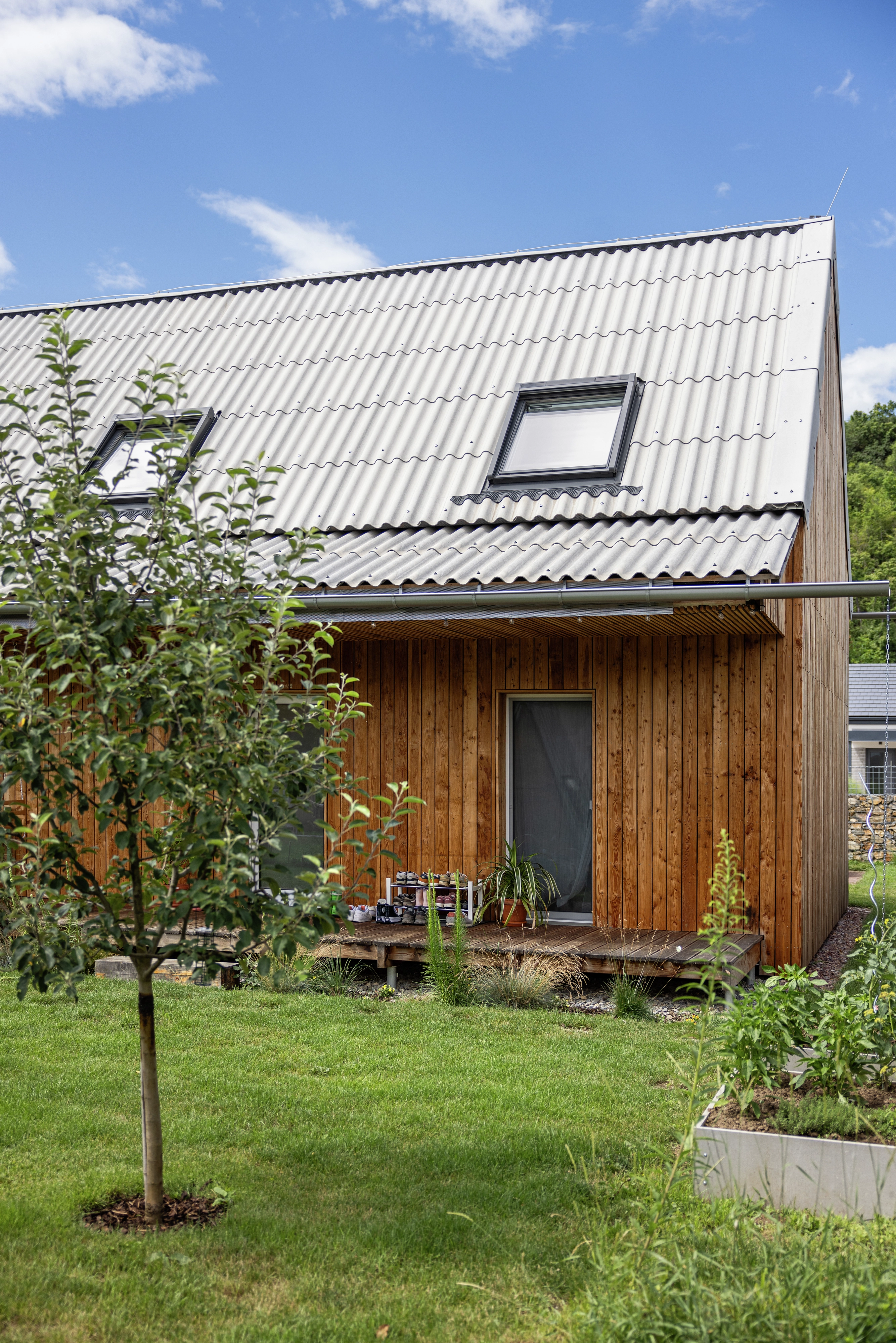 Wooden house with metal roof and VELUX roof windows, surrounded by garden.