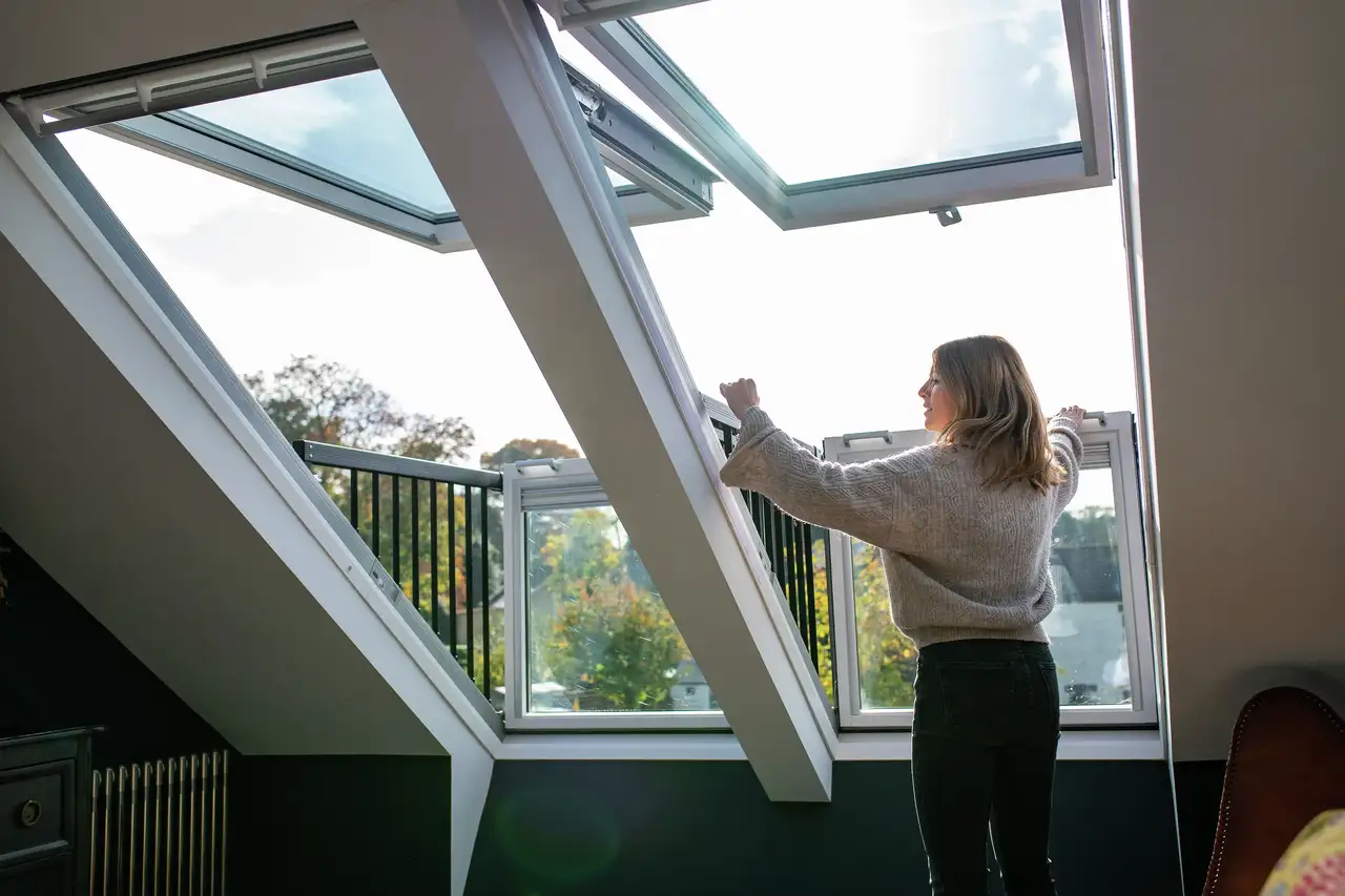 Woman opens VELUX roof balcony window to ventilate bedroom.