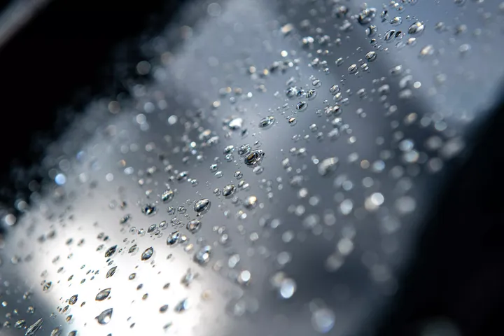 Nahaufnahme von glitzernden Regentropfen auf einer Glasoberfläche, die Licht reflektiert.