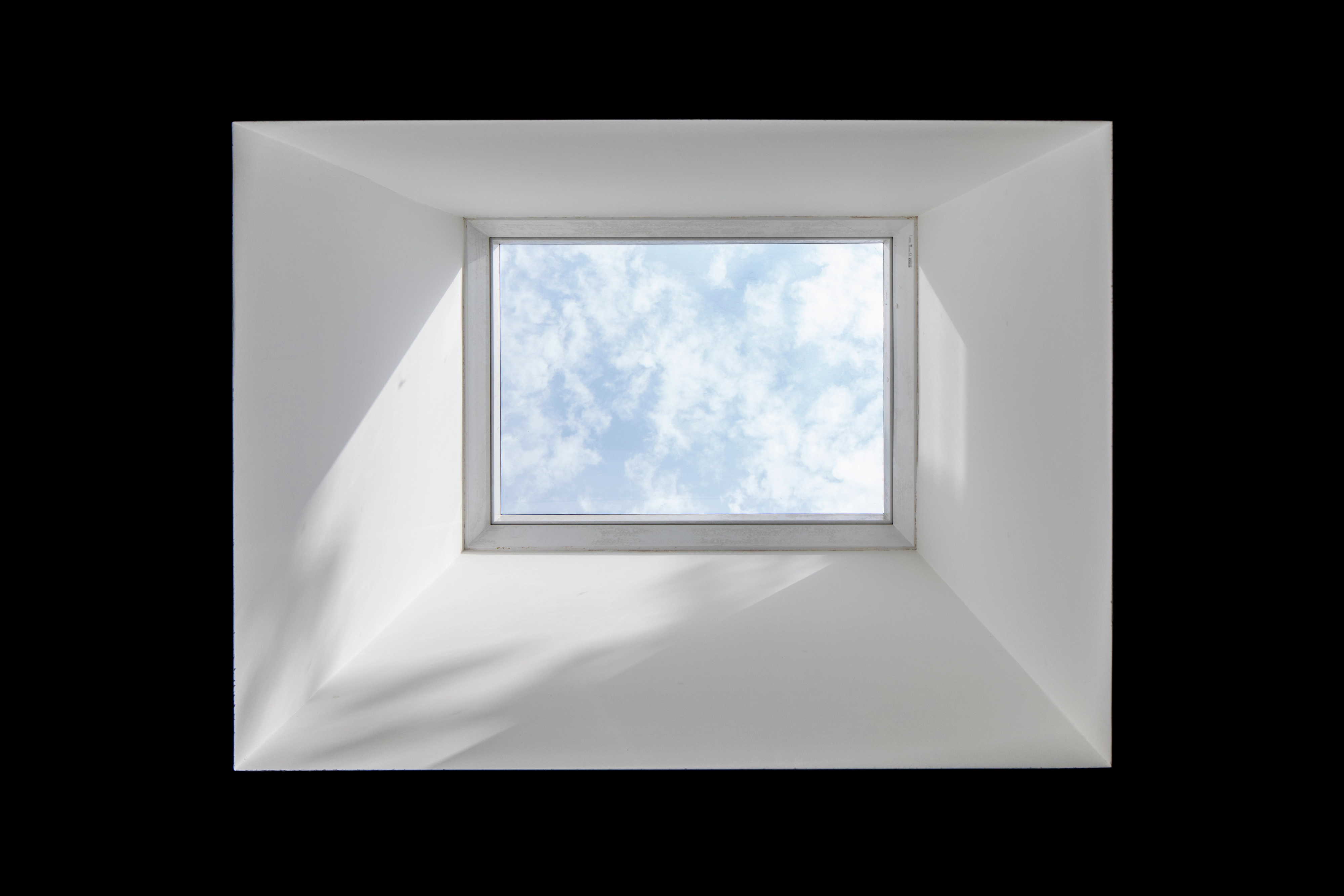 VELUX roof window with a view of blue sky and clouds.