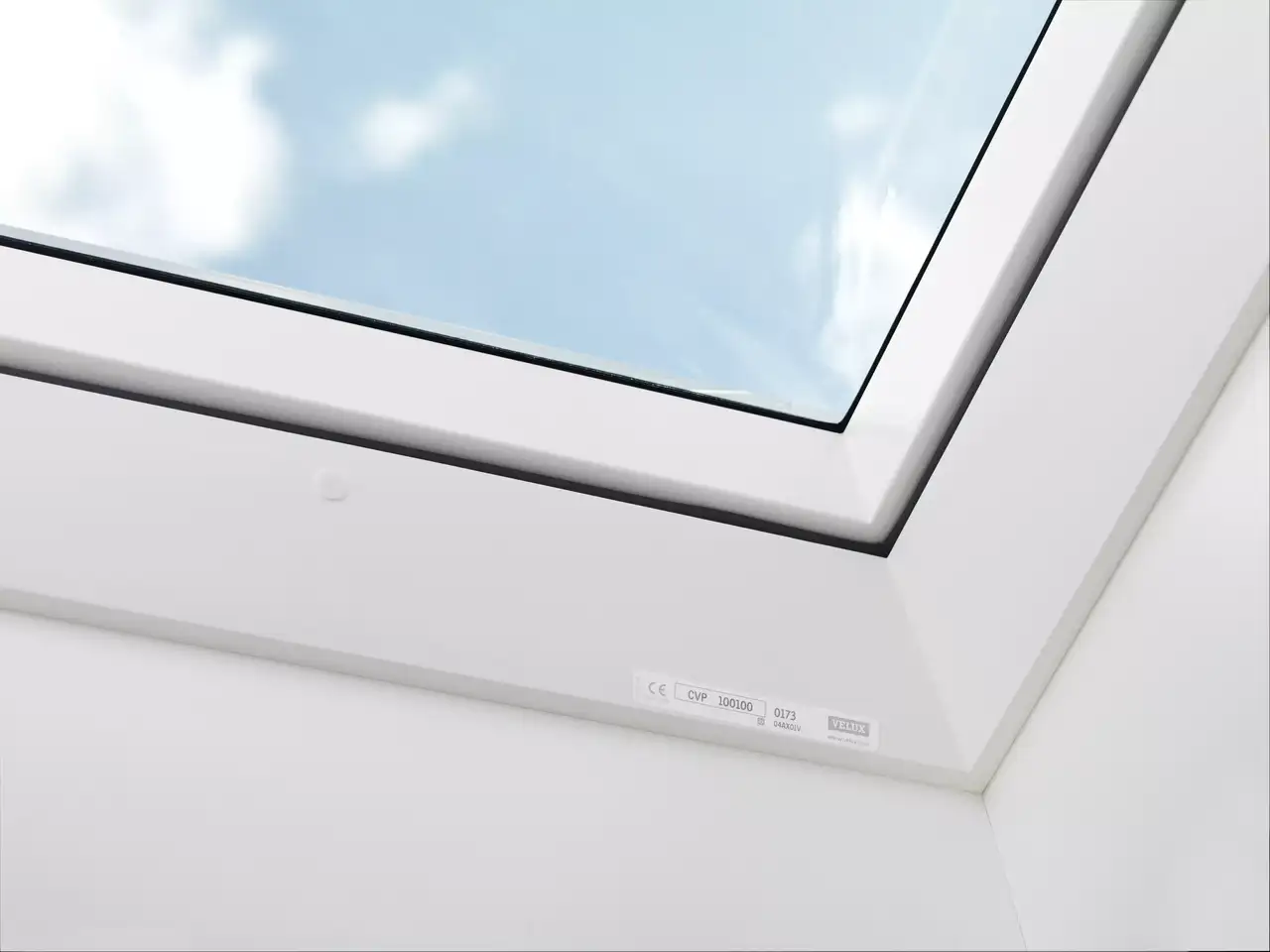 Modernes VELUX Dachflächenfenster in weißer Decke mit Aussicht auf blauen Himmel und Wolken.