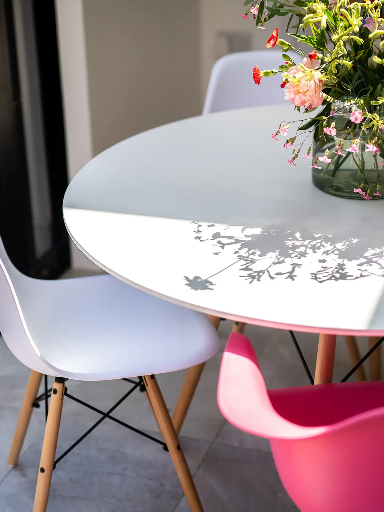 Table blanche entourée de chaises colorées, vase fleuri reflétant la lumière naturelle, ambiance Dopamine decor en cuisine 