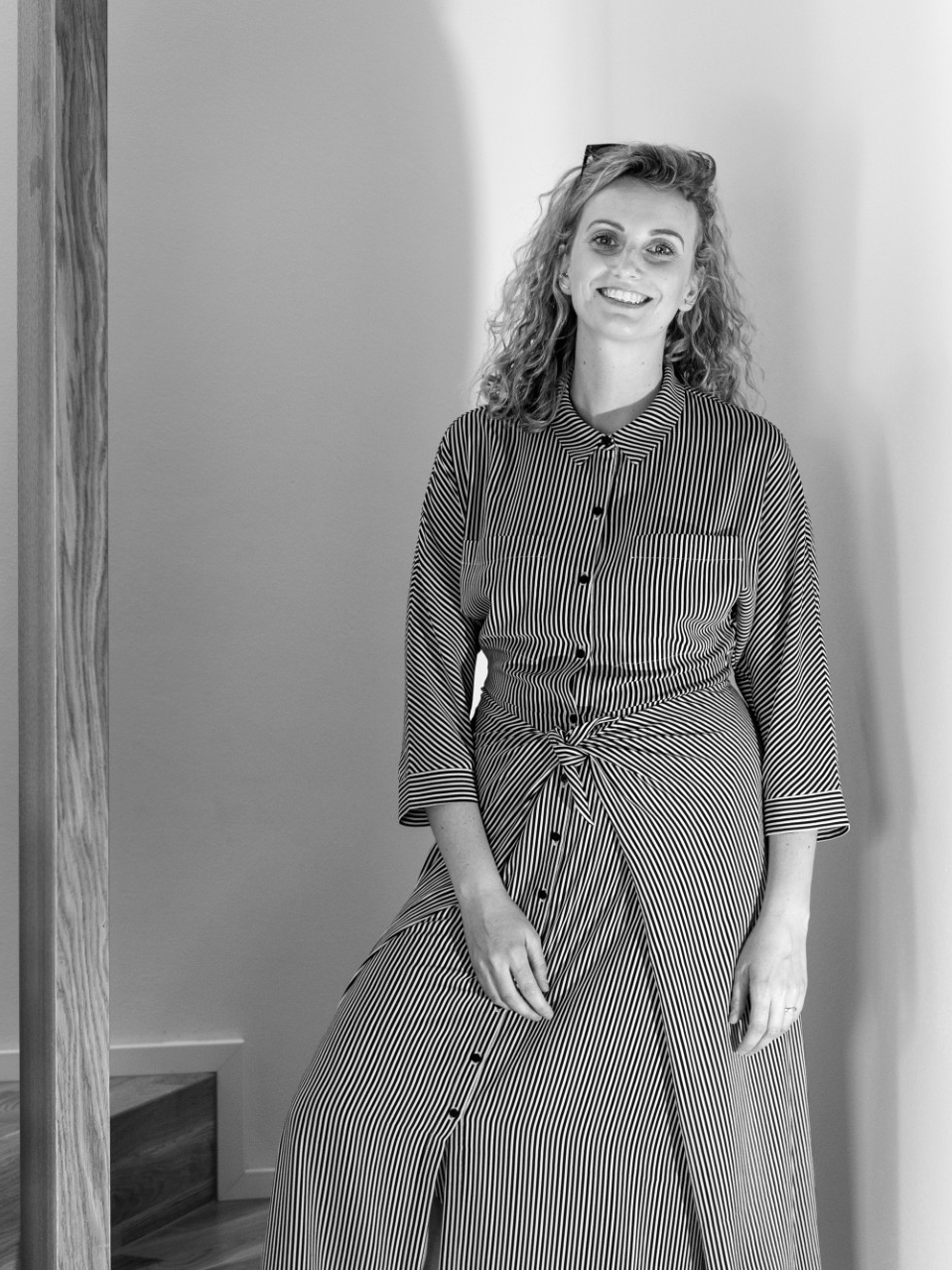 Person in striped dress by modern staircase with wooden railings.