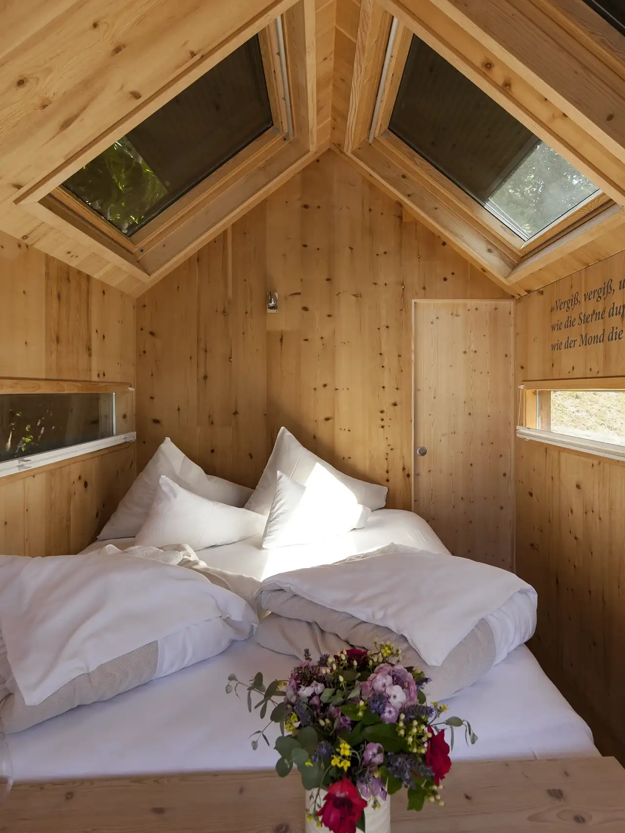 Camera da letto in mansarda con rivestimento in legno e due finestre per tetti con tapparella esterna in alluminio. 