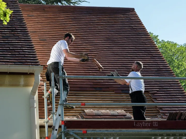 Двама работници сменят покривни керемиди на скеле. | VELUX 