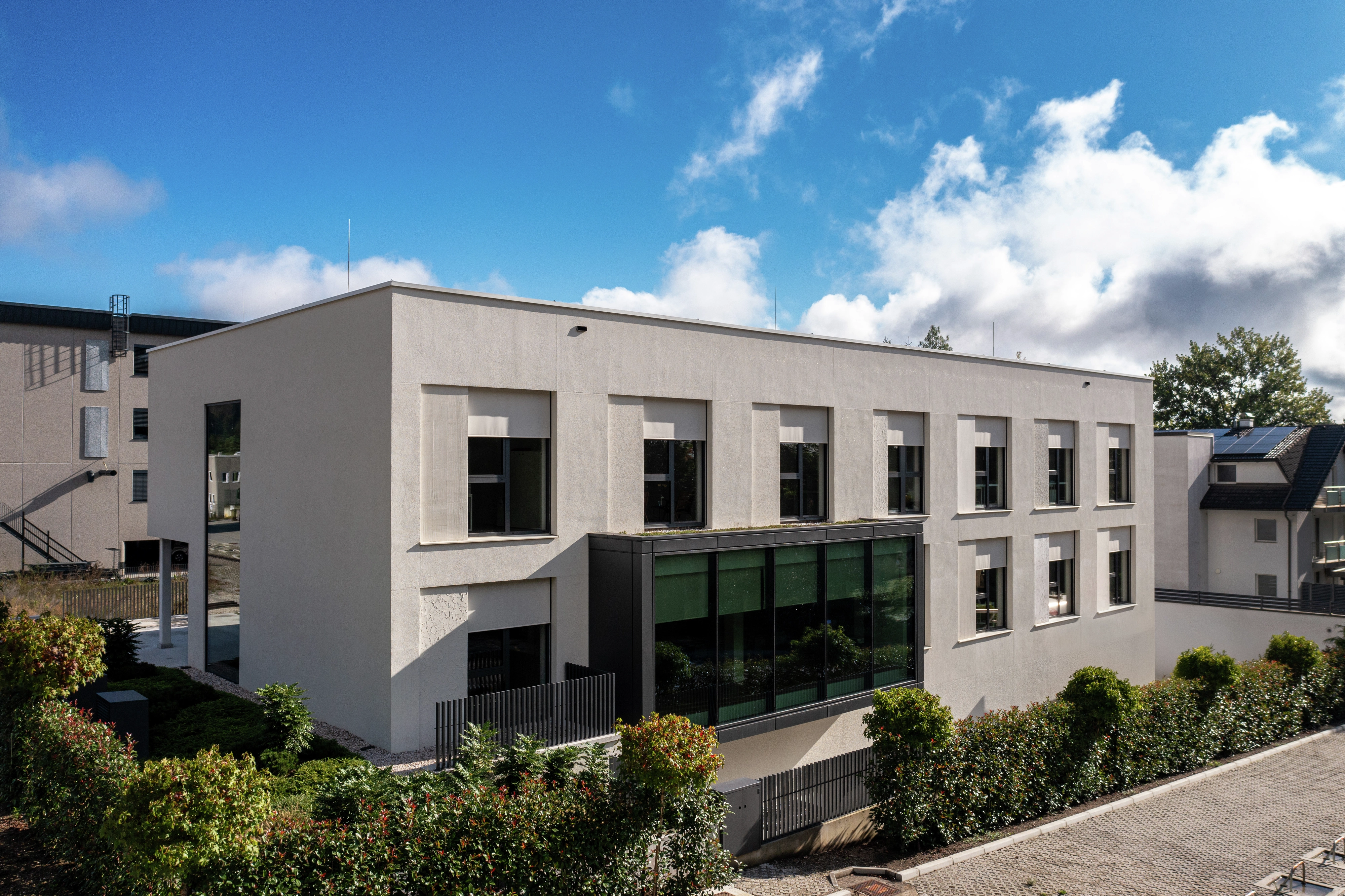 Moderní kancelářská budova s velkými okny a plochou střechou, obklopená keři