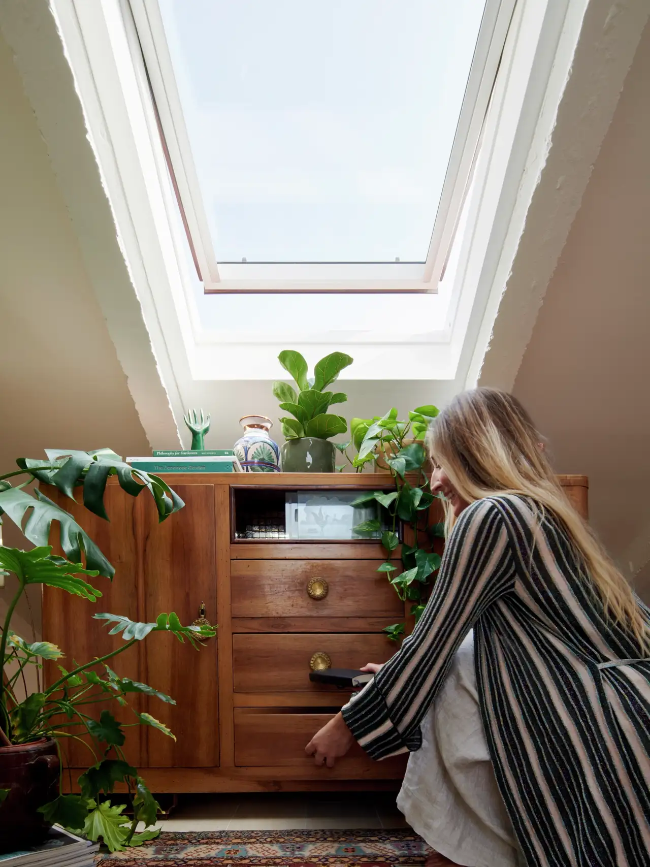 Attic room with VELUX roof window, plants, and wooden cabinet.