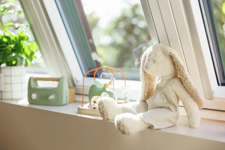 Plüschhase in sonnendurchflutetem Kinderzimmer mit VELUX Dachflächenfenster und Babyspielzeug.