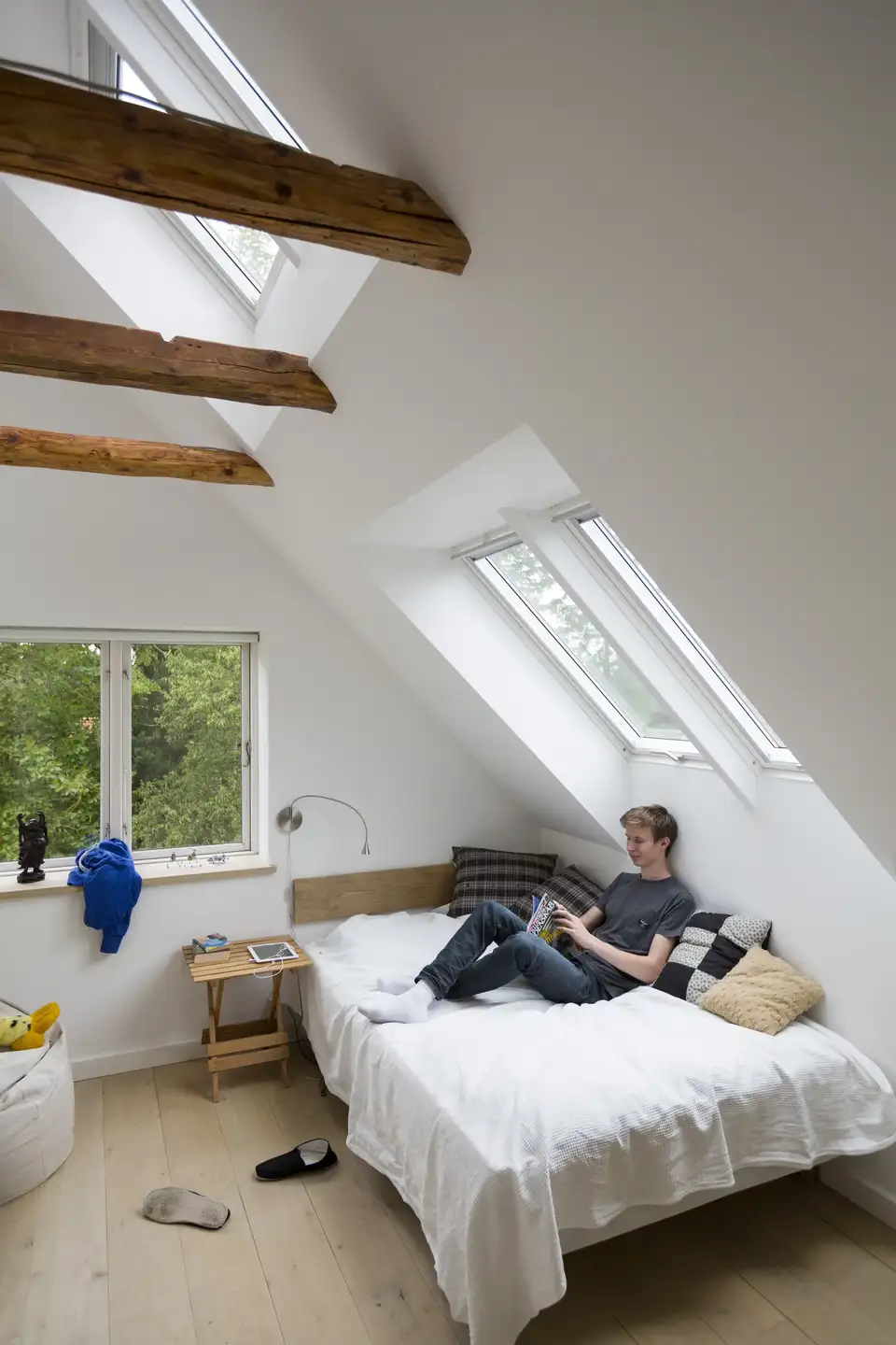 Quarto sob o telhado com uma grande janela de telhado que deixa entrar luz natural e valoriza os revestimentos em madeira