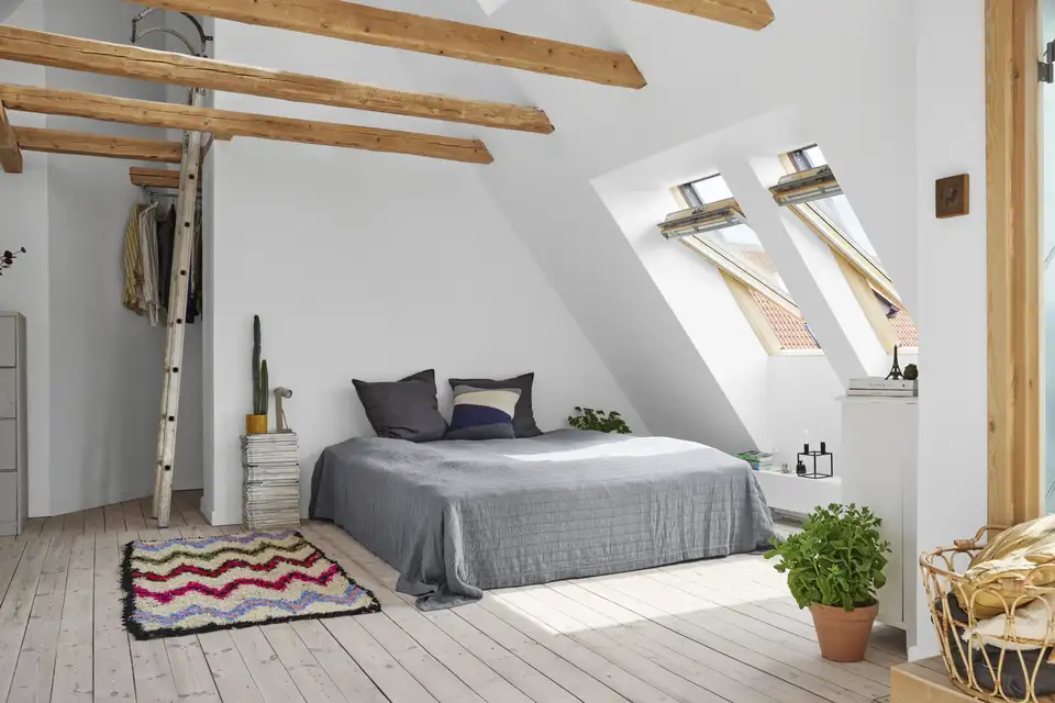 Priestranná podkrovná spálňa s odhalenými drevenými trámami a veľkými strešnými oknami | VELUX