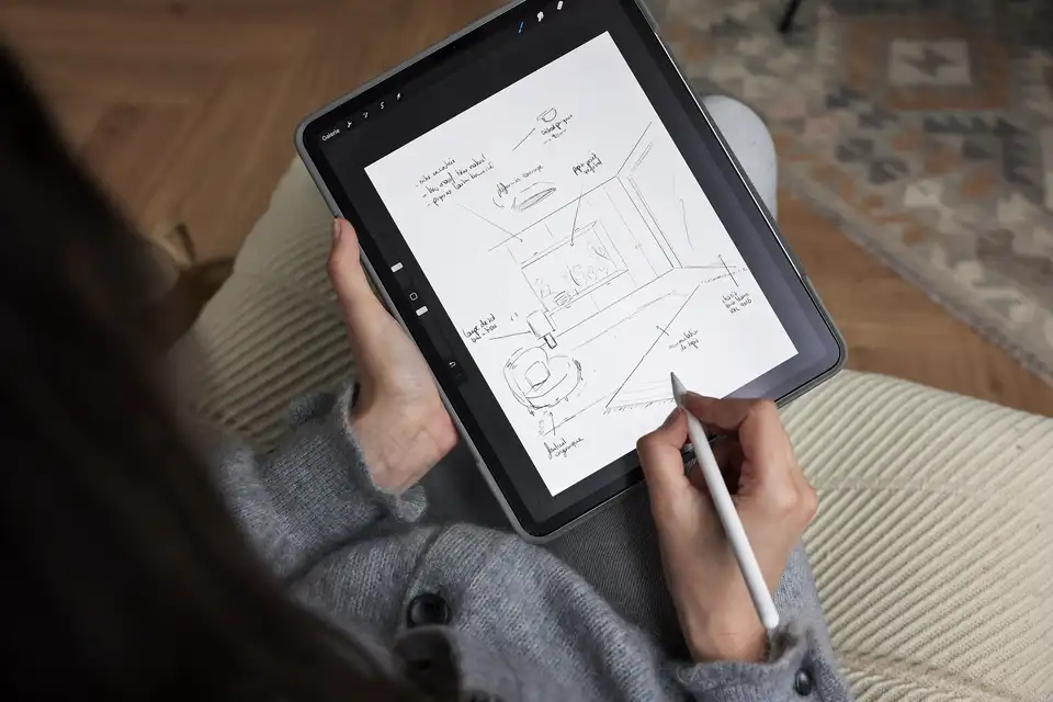 Person sketching living room design on tablet, cozy setting with rug and wooden floor. 