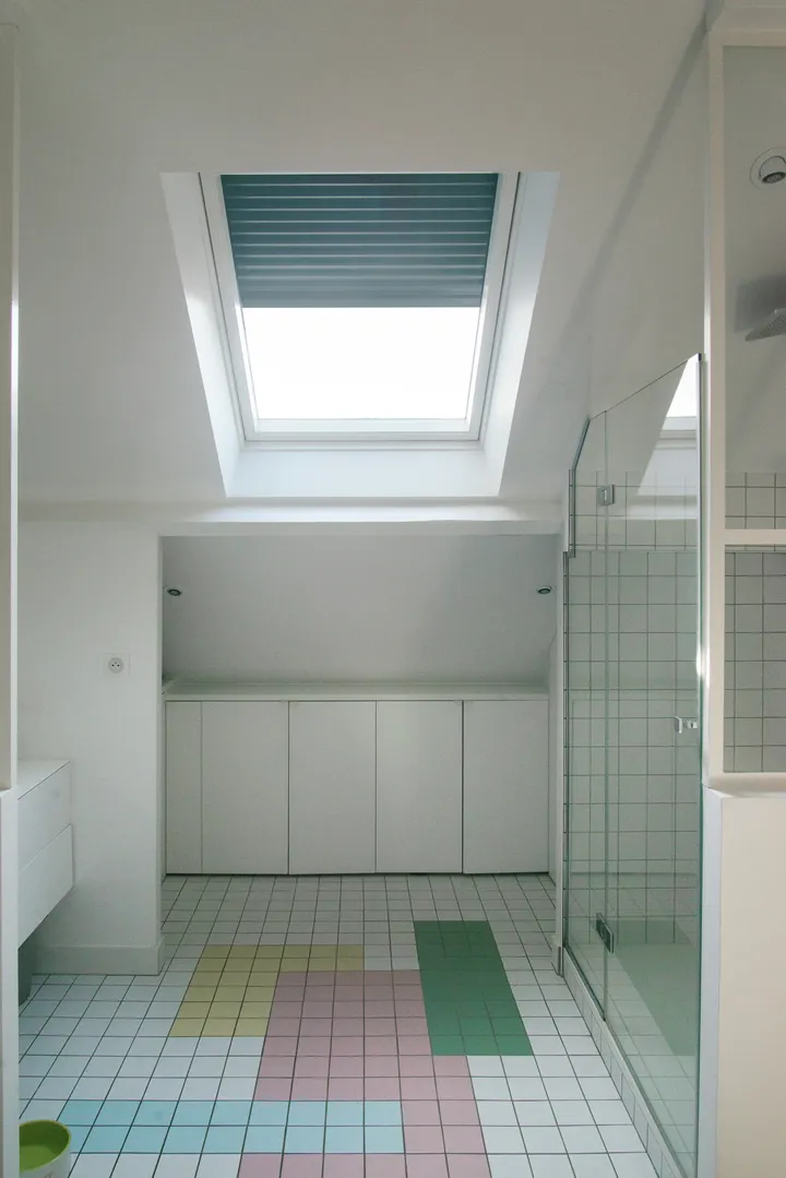 Баня с покривен прозорец VELUX, стъклен душ и цветни плочки.