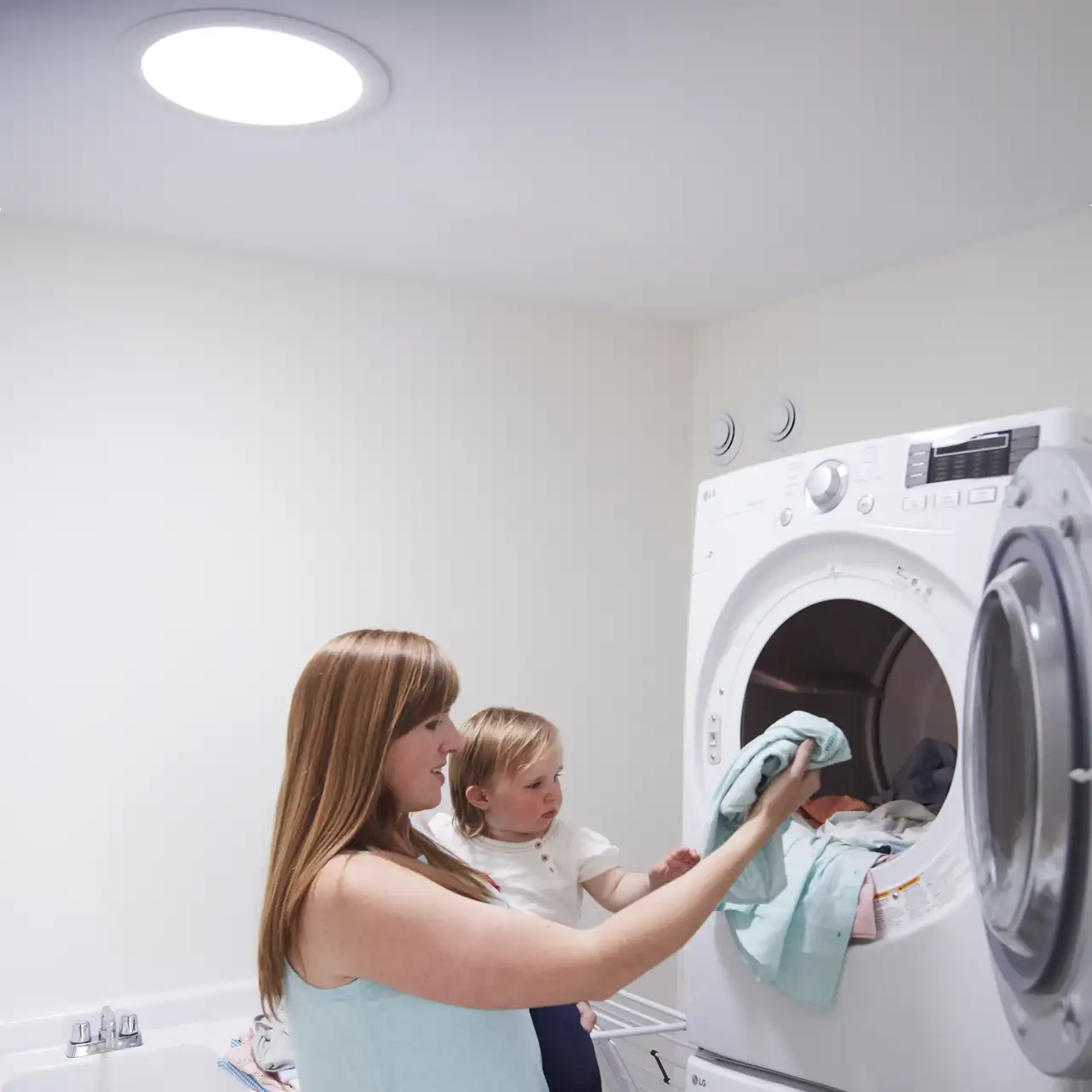 femme portant une petite fille dans les bras et sortant le linge sec du sèche-linge 
