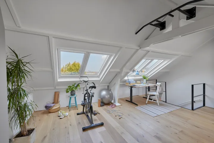 Таванско помещение със скосен таван, прозорци VELUX, фитнес уреди и бюро.