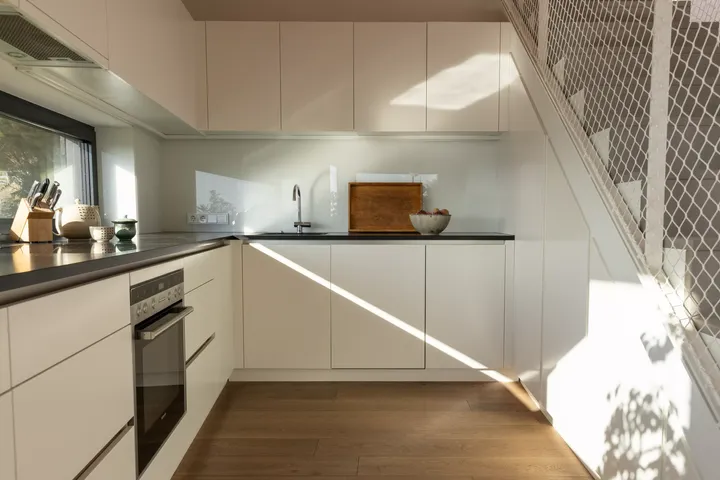 Moderne, sonnendurchflutete Küche mit weißen Schränken, Edelstahlgeräten und VELUX-Fenster.
