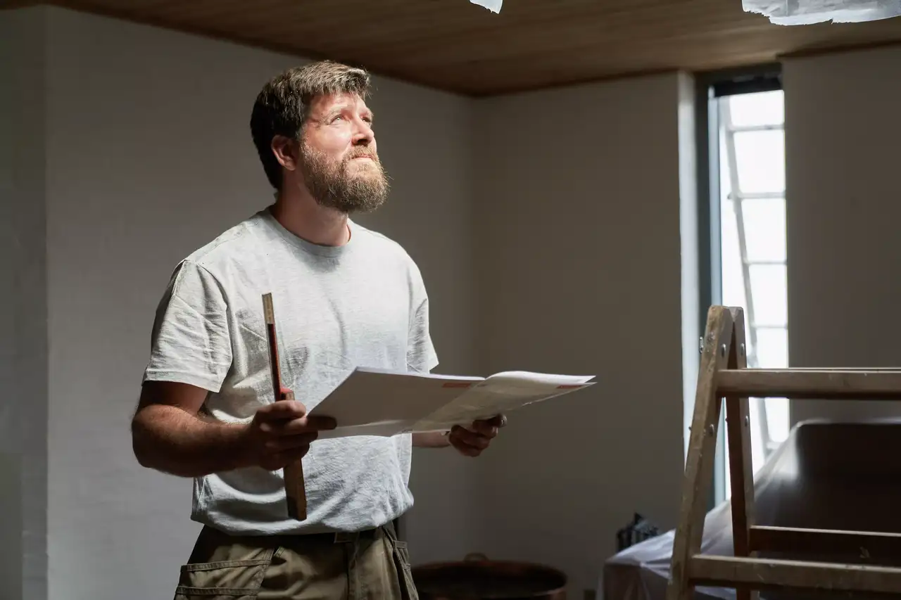 Dachdecker mit Zollstock und Baugenehmigung in der Hand prüft den Einbau der Dachfenster | VELUX Magazin