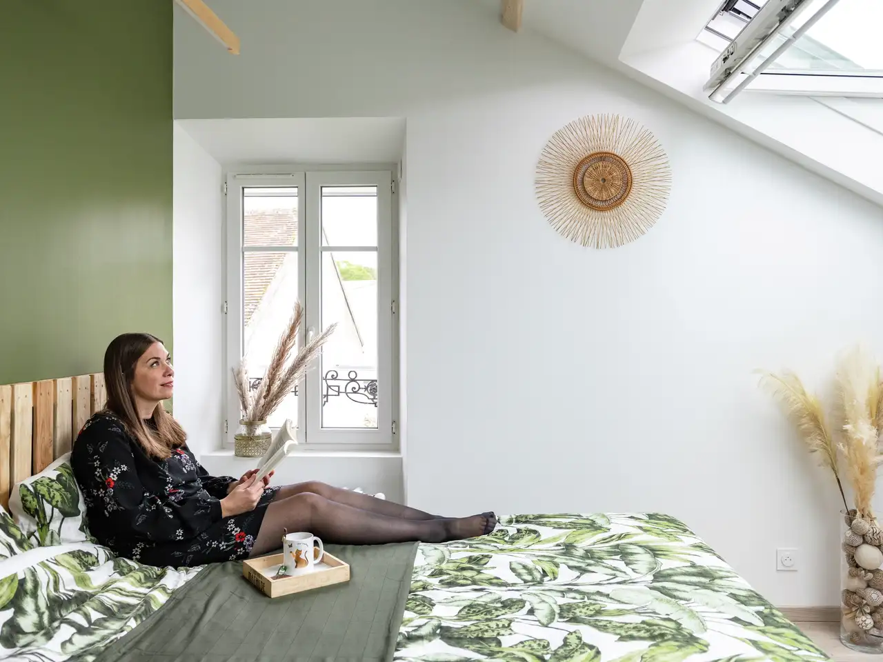 Una donna seduta sul suo letto guarda fuori attraverso una finestra per tetti VELUX.