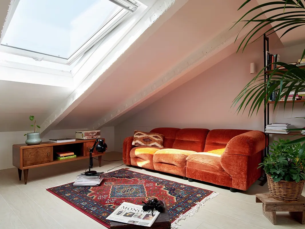 Salon lumineux sous les combles avec un canapé orange, un tapis persan et une fenêtre de toit VELUX.